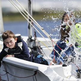 a group of children splashing water while sailing a dinghy