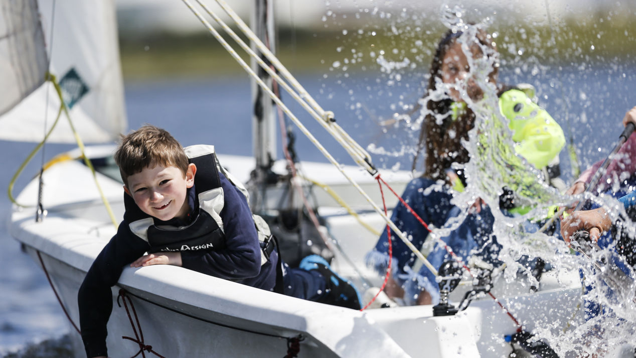 a group of children splashing water while sailing a dinghy