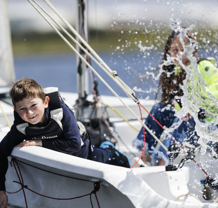 a group of children splashing water while sailing a dinghy