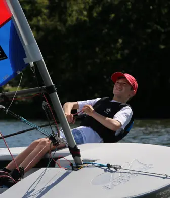 A boy leaning out of a sailing boat (hiking) while holding the controls to help steer it