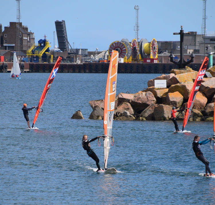 Long shot of group of youths, each on windsurfs 