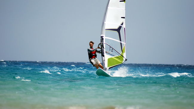 Long shot of man on windsurf with waves splashing