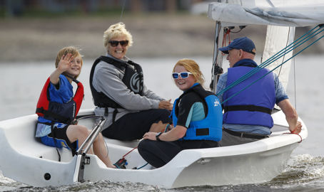 Mid shot of family sailing on a dinghy and smiling at camera
