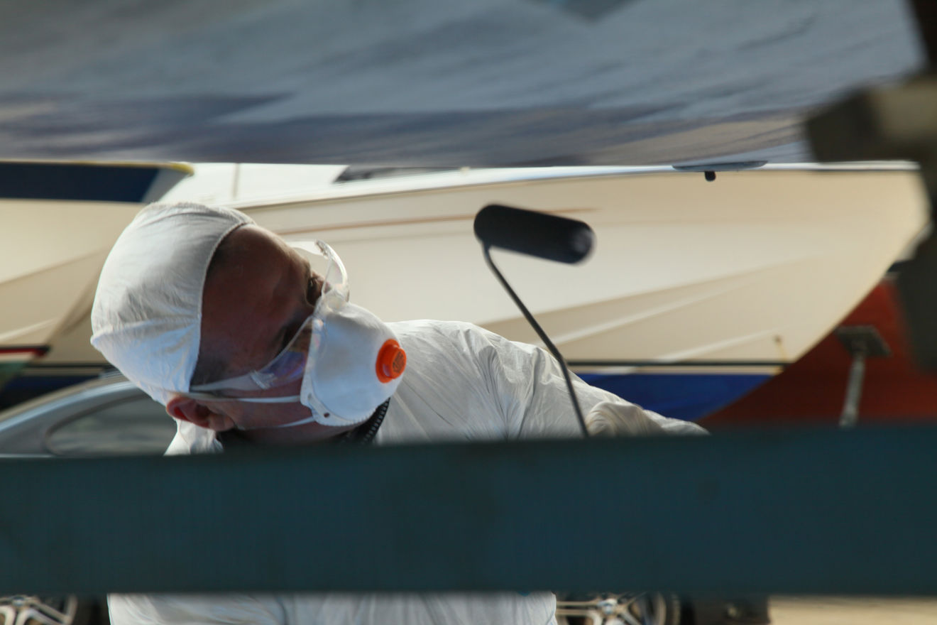 man in white protective clothing and mask, antifouling the underneath of his yacht
