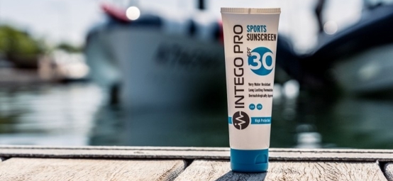 Intego Pro sunscreen on a waterside wooden deck in the sunshine with moored boats in the background.