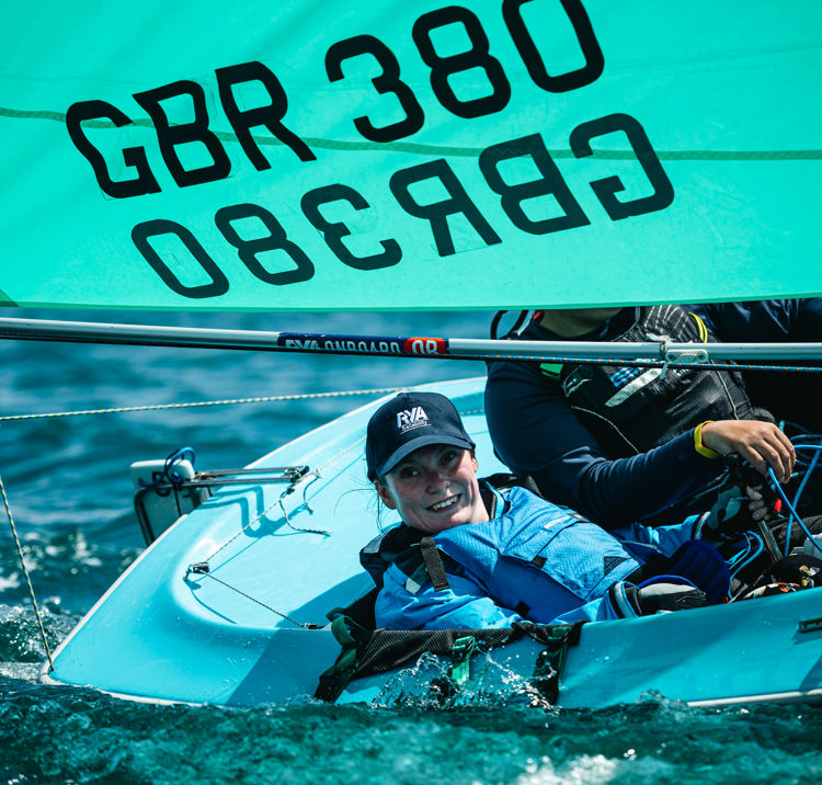 	A disabled woman helping a dinghy, sailing fast in the sun, with crew next to her