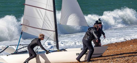 Long shot of sailors pulling catamaran onto the shore