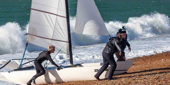 Long shot of sailors pulling catamaran onto the shore
