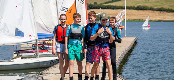 Children walking on a pontoon with dinghies in the background