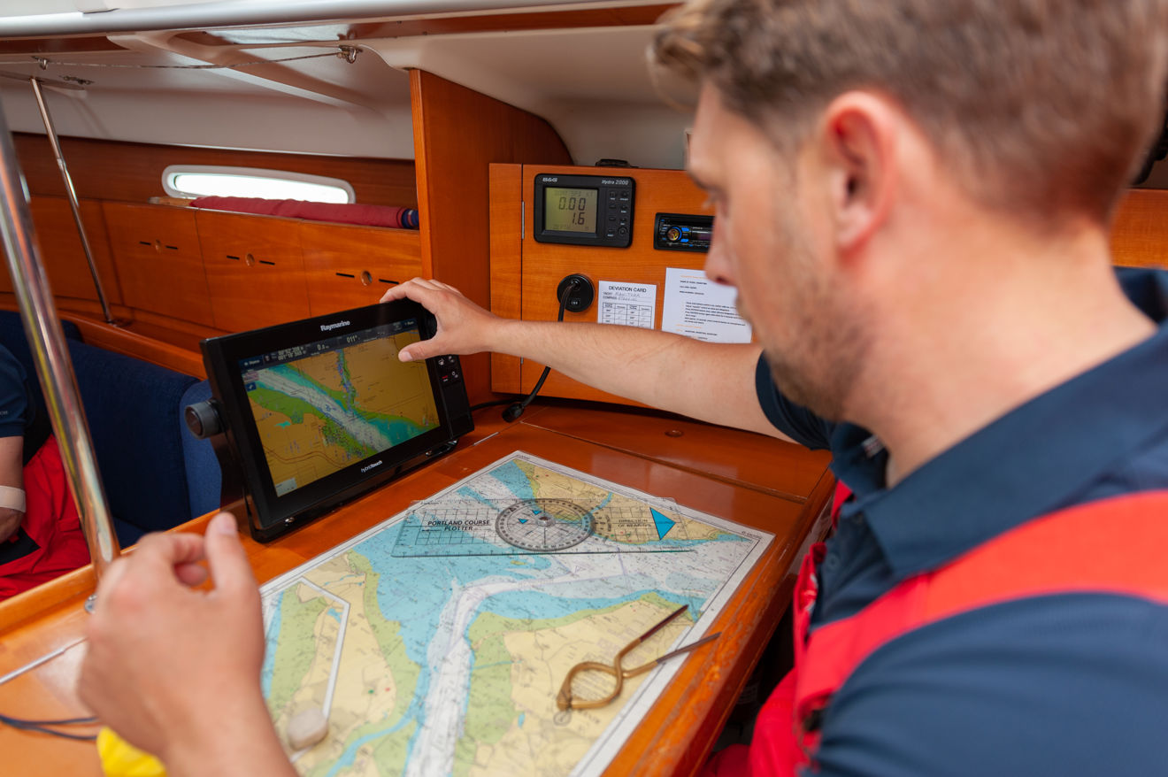 Man seated at chart table carrying out navigation on paper and electronic chart