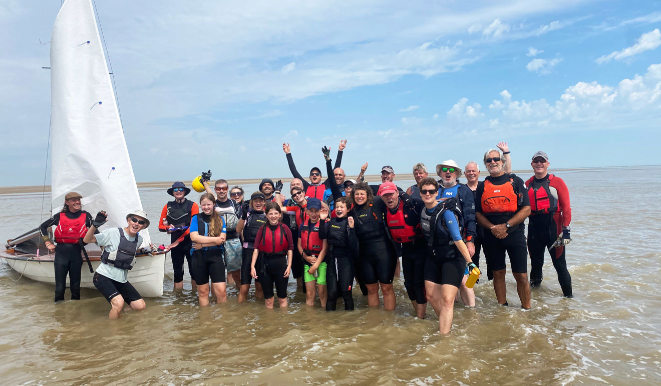 An image of Community photo sailing club group shot by the water with a boat