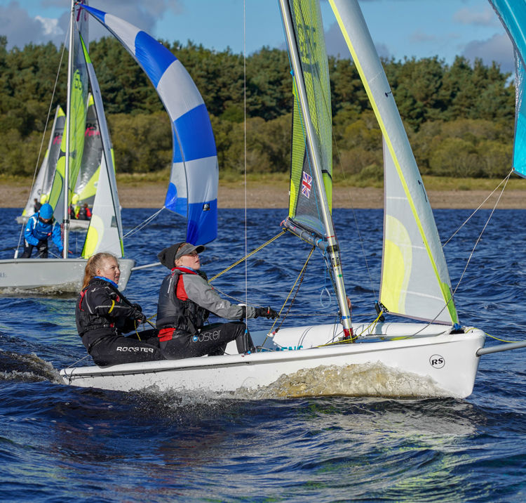 Long shot of two women sailing a small sailboat with other sailboats in the background